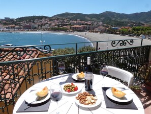 A table with food and drinks, overlooking a coastal town and beach. - Spacious duplex near the sea (Banyuls-Sur-Mer)