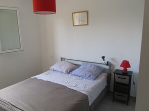 A simple bedroom with a bed, a bedside table, a lamp, and a framed picture on the wall. - New villa, 4 km from pinarello beaches, 3 bedrooms, small garden (Zonza)