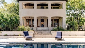 Une maison à deux étages avec une piscine, dotée d’un patio avec deux chaises longues et d’un escalier menant à l’entrée.
