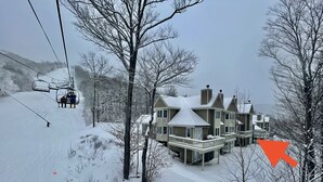 A large, multi-story house with a snow-covered roof, surrounded by trees and a ski lift in the background. - Sunday River Ski In Ski Out Locke Mountain condo with Pool Jacuzzi (Newry)