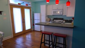 A kitchen with wooden flooring, white cabinets, a microwave, a stove, and two red bar stools.
