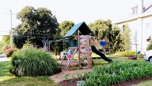 A playground with a climbing structure and slide, surrounded by grass and plants.