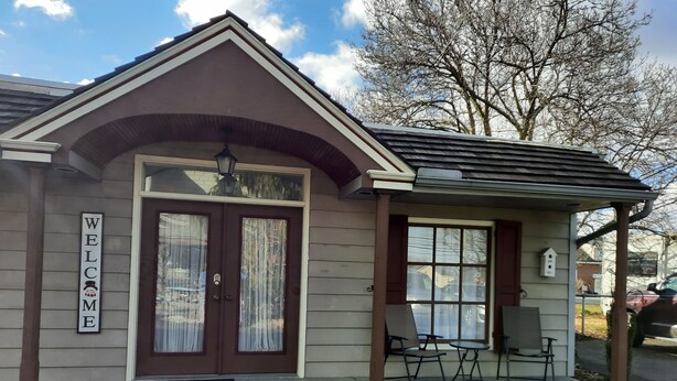 A small building with a 'WELCOME' sign, a porch with chairs, and a covered area with a table.