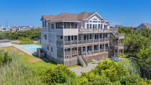 A multi-story building with balconies, a pool, and a deck area. - Premier Soundfront Home w/ Pool, HotTub, Elevator, Pickleball, Tiki Lounge, More (Rodanthe)
