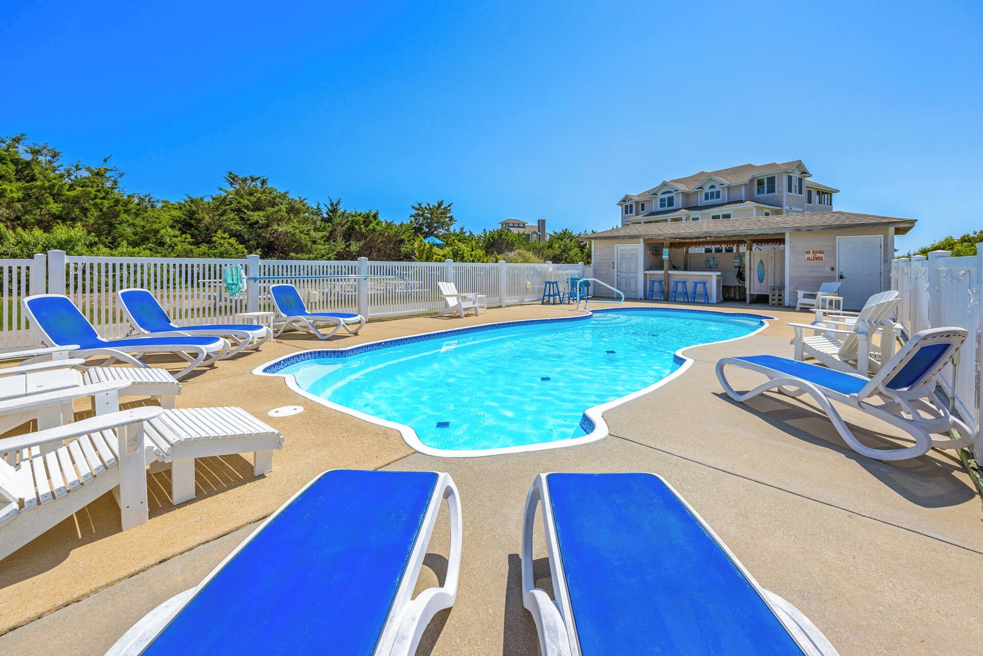 A swimming pool with blue and white lounge chairs, a fenced area, and a building with a 'No Diving Allowed' sign.