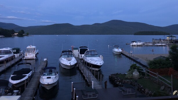 A marina with boats docked at wooden piers, surrounded by calm water and hills in the background. - Lake George and Adirondacks (Bolton Landing)