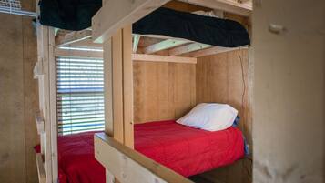A bunk bed room with wooden walls and a window with blinds.