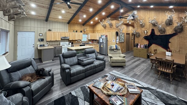 Amplia sala de estar con sofás de cuero, comedor con sillas de madera, cocina con electrodomésticos modernos y ventilador de techo.