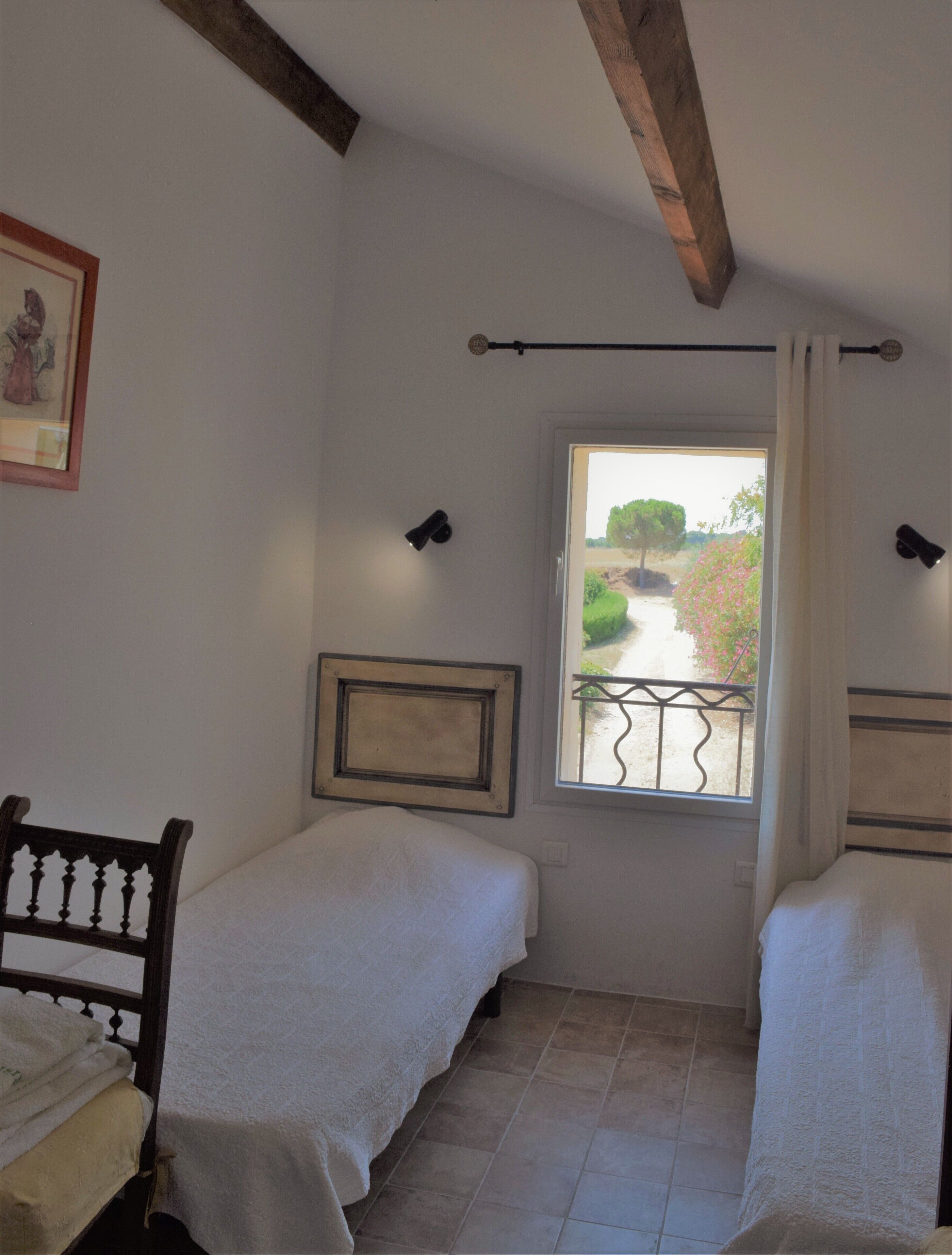 Quarto pequeno e bem iluminado com duas camas, uma janela com vista para um jardim e um quadro na parede.