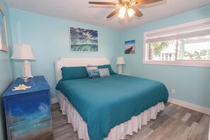 A bedroom with a bed, two bedside tables, a ceiling fan, and a window with a view. - Serene deck retreat w/ Gulf Views in west end PCB (Panama City Beach)