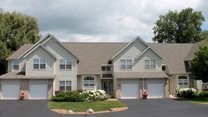 A two-story house with a central entrance, two garages, and a landscaped front yard with flowers and shrubs.
