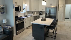 A modern kitchen with white cabinets, stainless steel appliances, a central island with bar stools, and pendant lighting.