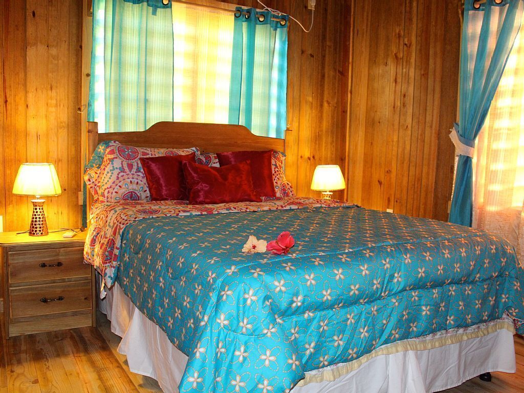 Una habitación con paneles de madera, una cama, dos lámparas de noche y un ventanal con cortinas.