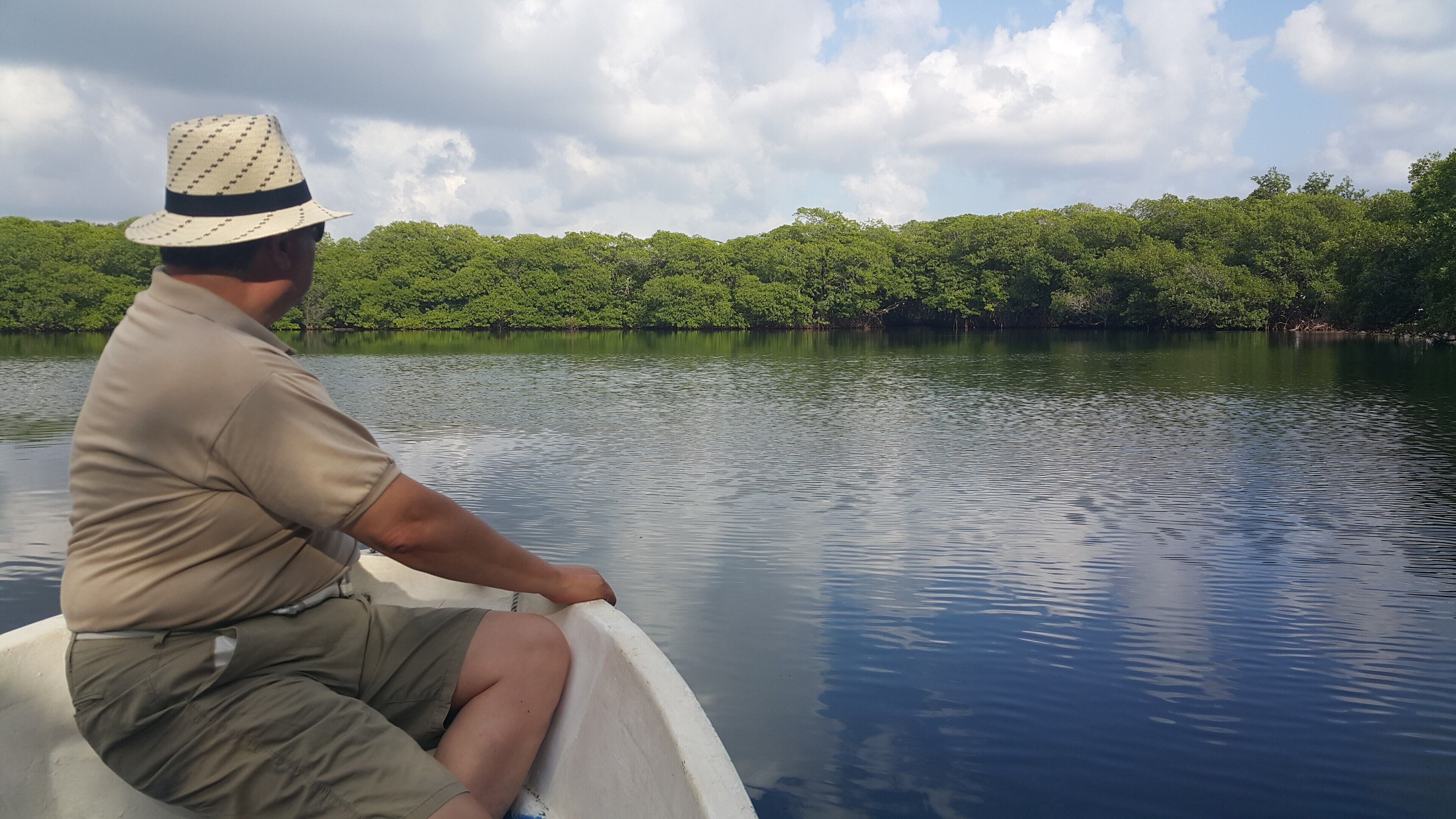 Un homme dans un bateau sur un lac paisible, avec une végétation luxuriante en arrière-plan.