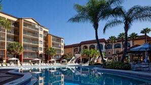 A hotel with a swimming pool, palm trees, and a covered outdoor seating area.