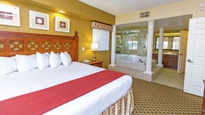 A hotel room with a large bed, a bathroom with a bathtub, and a view of the kitchen area.