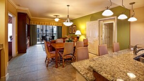 A spacious kitchen with a granite countertop, dining area with wicker chairs, and pendant lighting.