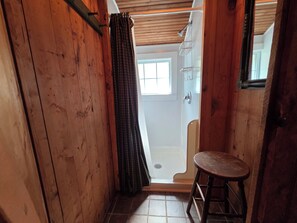 A narrow wooden hallway with a door leading to a bathroom, a small stool, and a metal rack with hooks. - Detox Cottage ▪︎ BYO Linens & Unplug (Mount Gretna)