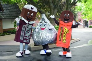 Three mascots dressed in chocolate-themed costumes standing on a paved area with trees and buildings in the background. - Detox Cottage ▪︎ BYO Linens & Unplug (Mount Gretna)