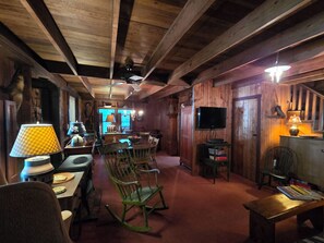 A rustic interior with wooden beams, a dining area with chairs and a table, a television mounted on the wall, and a fireplace. - Detox Cottage ▪︎ BYO Linens & Unplug (Mount Gretna)