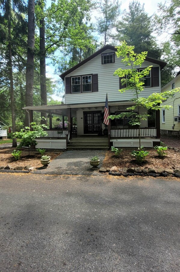 A two-story house with a porch, a small garden, and an American flag. - Detox Cottage ▪︎ BYO Linens & Unplug (Mount Gretna)