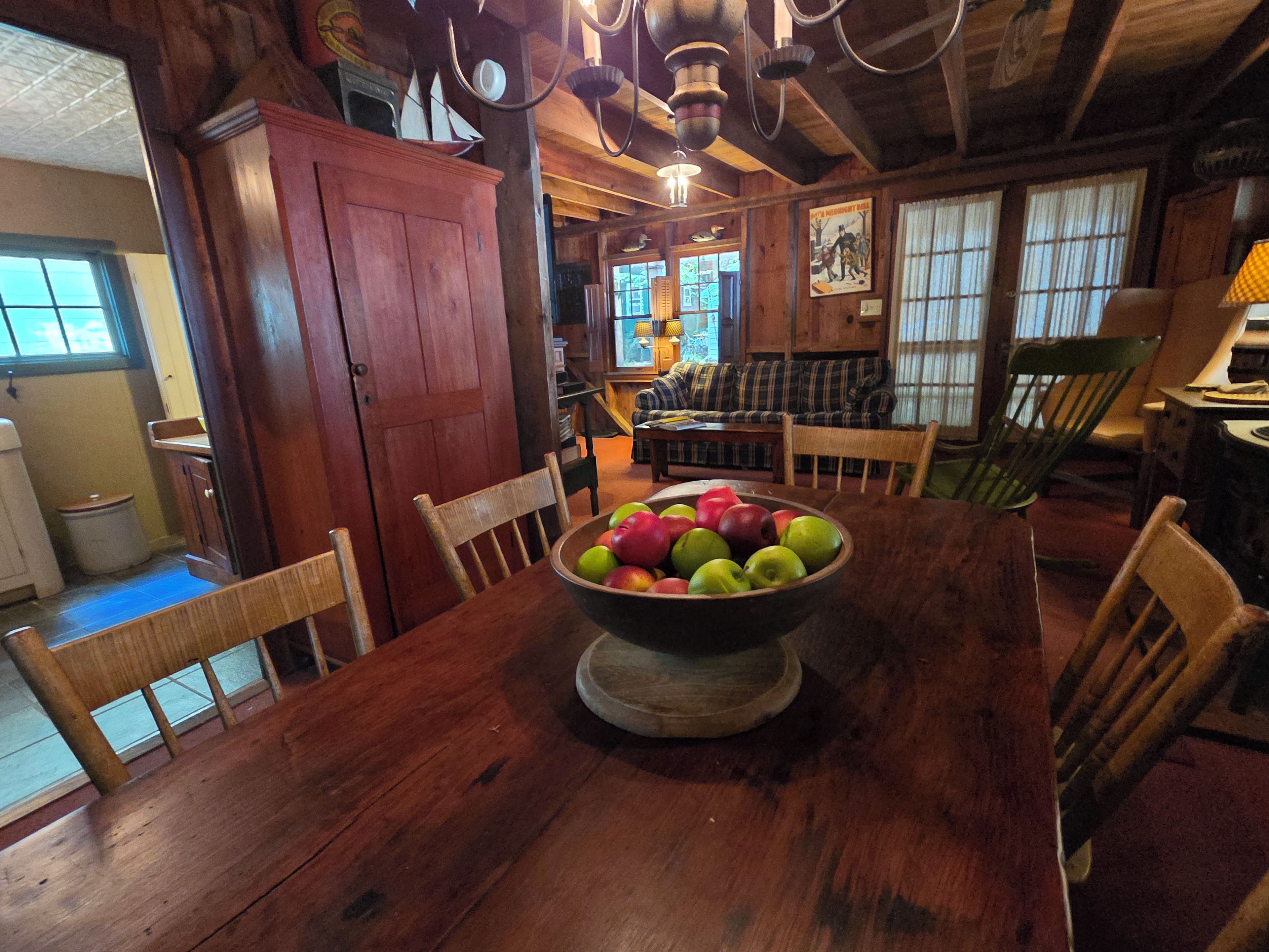 A wooden dining table with a bowl of fruit in the center, surrounded by chairs.