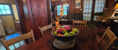 A wooden dining table with a bowl of fruit in the center, surrounded by chairs.