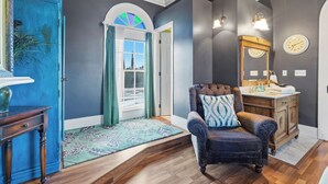 Una habitación con puerta azul, una silla de madera con cojín estampado, un armario de madera y un espejo con reloj.