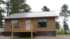 Une petite cabane en bois avec un toit en métal, une terrasse en bois et de grandes fenêtres.