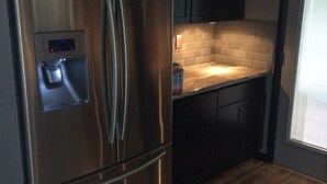 Ein Edelstahl-Kühlschrank mit Wasserspender, dunkle Holzschränke, eine helle Spritzschutzwand und ein Holzboden.