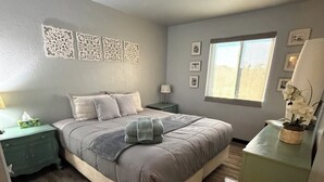 Ein Schlafzimmer mit Bett, Nachttisch, Kommode, Fenster und Wanddekoration.