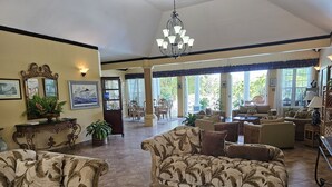 A spacious living area with multiple seating options, including sofas and chairs, a glass coffee table, and a chandelier. - Spicy Hill Villa, One Of Jamaica's Best-Kept Secrets. (Port Antonio)