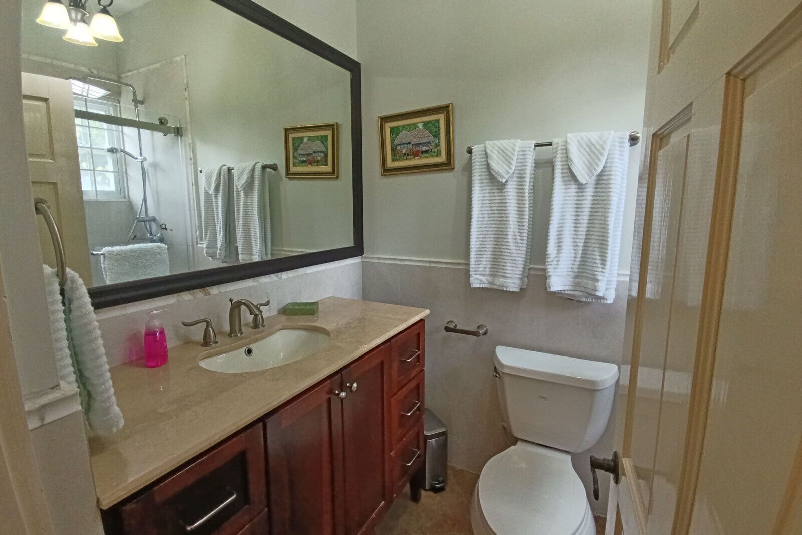Une salle de bain avec deux lavabos, des toilettes, un miroir et deux tableaux encadrés au mur.
