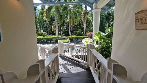 A wooden staircase leading to an outdoor patio area with white railings, surrounded by lush greenery and a sign that reads "Spicy Portland." - Spicy Hill Villa, One Of Jamaica's Best-Kept Secrets. (Port Antonio)