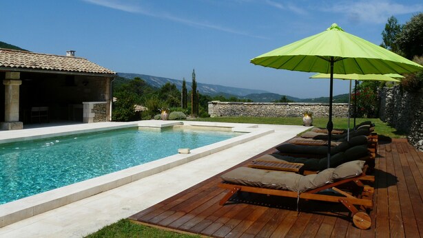 Un espace piscine doté d’une terrasse en bois, de chaises longues et d’un parasol vert.