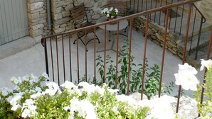 Un bâtiment en pierre avec une petite fenêtre, un banc en bois et une rambarde en métal.