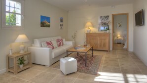 A living room with a white sofa, a wooden coffee table, a small side table with a lamp, and a large window. - "L'Olivaie side Garden" (Saint-Paul-De-Vence)