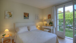 A bedroom with a large bed, a desk, and a window with a view of a garden. - "L'Olivaie side Garden" (Saint-Paul-De-Vence)