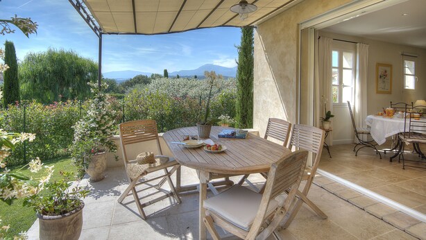 An outdoor patio with a wooden table and chairs, surrounded by potted plants and a view of a mountainous landscape. - "L'Olivaie side Garden" (Saint-Paul-De-Vence)