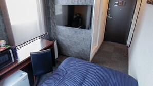 Een hotelkamer met een bed, een bureau met stoel, een magnetron, een koffiezetapparaat, een televisie en een deur met bedieningspaneel.