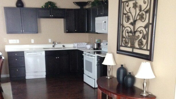A kitchen with dark cabinets, a white stove, and a dining area with a table and two lamps. - Beautiful 2 Bedroom Luxury Loft in the heart of Aurora (Aurora)