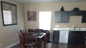 A dining area with a table and chairs, a kitchen with dark cabinets and a dishwasher, and a large window providing natural light. - Beautiful 2 Bedroom Luxury Loft in the heart of Aurora (Aurora)