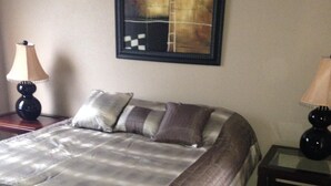 A neatly made bed with a striped bedspread, two bedside lamps, and a framed abstract painting on the wall. - Beautiful 2 Bedroom Luxury Loft in the heart of Aurora (Aurora)