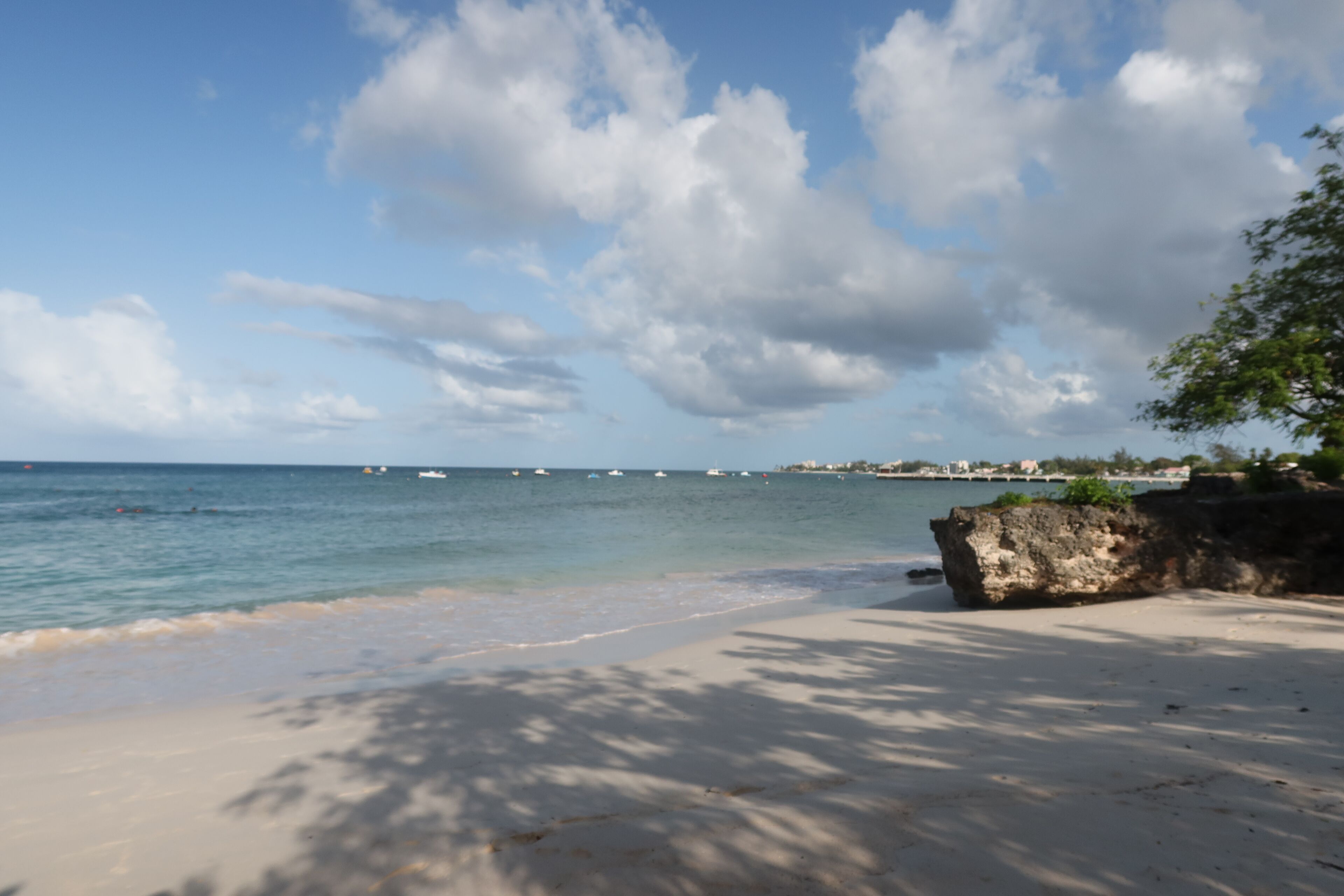 A beach with clear skies, calm water, and boats in the distance.