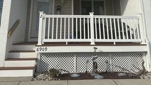Een gebouw met twee verdiepingen, een witte gevel, een veranda met een witte balustrade en een kleine tuin met decoratieve stenen en planten.
