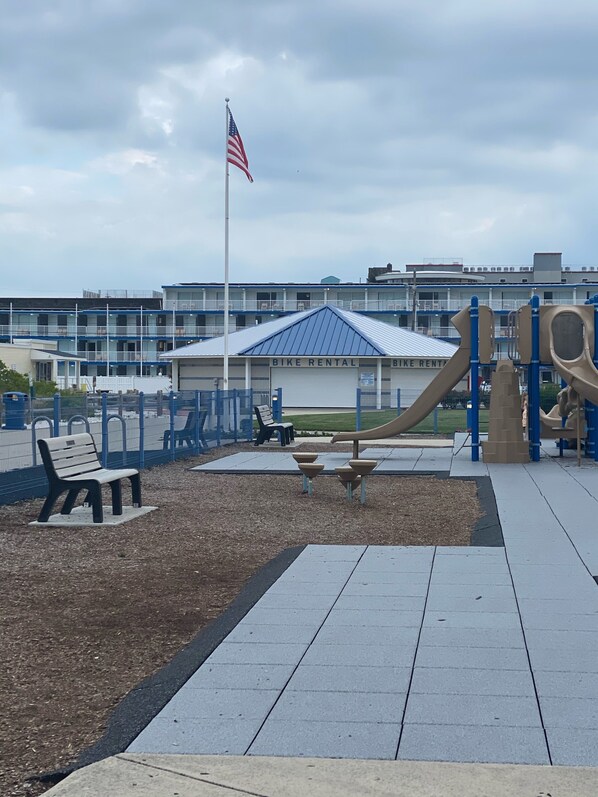 Un parque infantil con un tobogán y un edificio de alquiler de bicicletas al fondo.