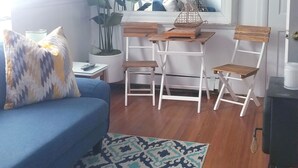 A living room with a blue sofa, a patterned rug, a wooden table with chairs, a potted plant, and a mirror above the table. - Town walking distance-Bridgehampton Cottage (Bridgehampton)