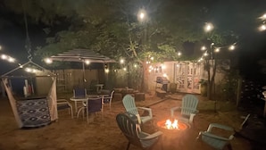 An outdoor seating area with chairs and a fire pit, surrounded by string lights and trees. - Town walking distance-Bridgehampton Cottage (Bridgehampton)