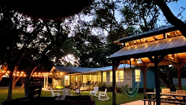 Un espace extérieur aménagé en patio, doté d’un coin salon couvert, d’un barbecue et de guirlandes lumineuses.