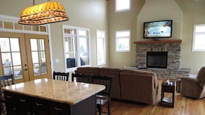 A spacious living room with a stone fireplace, a large TV mounted above it, and a cozy seating area with a sofa and recliner.